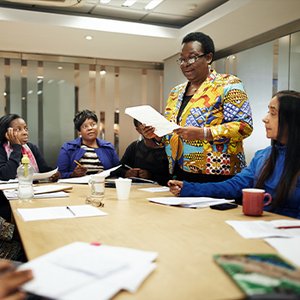 Woman facilitator standing up and presenting to three women around a table