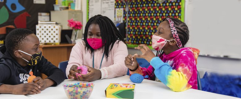 Three students around a table wearing masks