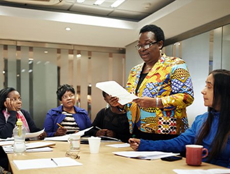 Woman facilitator standing up and presenting to three women around a table